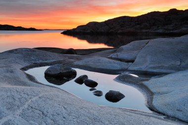 İsveç 'in Göteborg yakınlarındaki kıyı kayalarının üzerinde güneş batarken gökyüzünü canlı renkler kaplıyor. Sakin sular parlak renkleri yansıtır, sakin bir atmosfer yaratır..