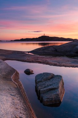 Gün batımında, Göteborg yakınlarındaki kıyı manzarası pembe ve turuncu renkleri yansıtan sakin suları ortaya çıkarır. Kayalık oluşumlar ve uzak tepeler akşam yürüyüşleri için mükemmel sakin bir atmosfer yaratır..