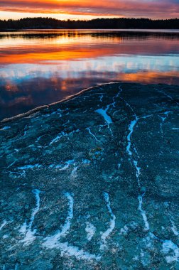 Sabahın erken saatlerinde İsveç 'teki dingin bir göl üzerinde ılık bir parıltı oluşur. Sakin sularda ve kayalarda yansıyan canlı renkler....