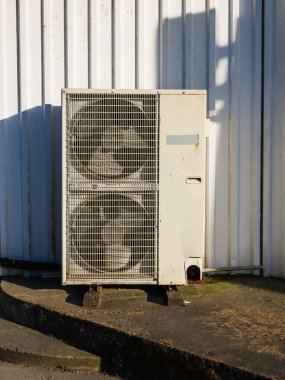 İsveç 'te beton bir levhanın üzerindeki bir duvarın yanında eski bir havalandırma ünitesi duruyor. Güneş ışığı, yıpranmış dış görünüşünü ve yaşlanan tasarımını vurgulayan bir gölge yaratır..