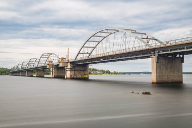 Gösterişli bir köprü İsveç 'te sakin bir nehir boyunca uzanır ve modern tasarımı doğal manzarayla harmanlar. Yeşillik, bölgenin barışçıl atmosferini yansıtan bankaların sınırlarını çiziyor..