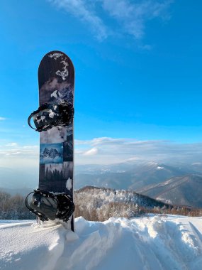 Dağın tepesinde kar kayağı sıkışmış. Güzel dağlar ve arkadaki mavi gökyüzü. Güneşli bir hava. Aktif eğlence, tatil köyünde snowboard. 