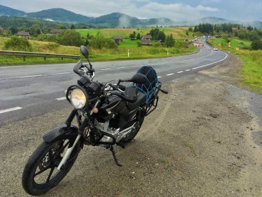 Motosiklet seyahatleri ilkbaharda, yazda, sonbaharda. Kırsal, doğa, dağlar, arka planda mavi gökyüzü. Mola için yolun kenarına park edilmiş siyah motosiklet. Ekstrem, eğlence, eğlence, yaşam tarzı.