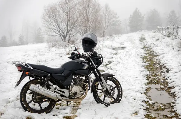 Motosiklet kışın seyahat eder. Kırsal, doğa, ağaçlar ve arkada sis. Mola için off-road 'a park edilmiş siyah motosiklet. Bir sürü beyaz kar var. Ekstrem, eğlence, yaşam tarzı