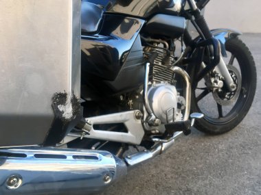 Düştükten sonra siyah motosiklet asfalta park etmiş. Trafik kazası. Panniers veya yan çantalarda darbe ve fren izleri var. Çelik bavullar. Kargo taşımacılığı.