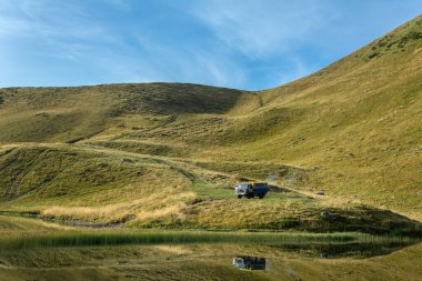 Dragobrat Dağları, Transcarpathia, Ukrayna. Dogoyaska ya da Gerisaska Gölü yakınlarında yeşil çimlere park etmiş bir kamyon. Seyahat, dağ gezileri, off-road sürüşleri. Güneşli hava ve bulutlu gökyüzü.