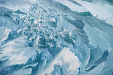 Yakın plan bir buz dokusu kısmen karla kaplı. Yüzeyde, narin çatlaklar ve buz gibi kenarlarla karışık donmuş desenler sergiliyor. Yumuşak, tozlu kar etrafa saçılmış..