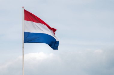 Hollanda bayrağı rüzgârda dalgalanıyor. Kırmızı, Beyaz ve Mavi. Ulusal gurur ve birlik. Hollanda 'daki vatanseverlik ruhu. Arka planda gökyüzü, su veya binalar.