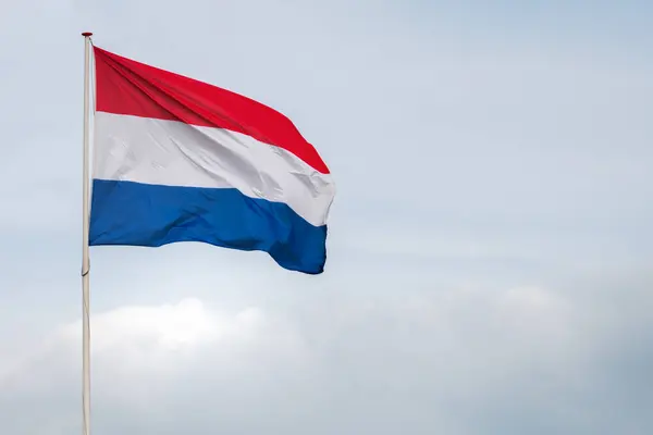 Hollanda bayrağı rüzgârda dalgalanıyor. Kırmızı, Beyaz ve Mavi. Ulusal gurur ve birlik. Hollanda 'daki vatanseverlik ruhu. Arka planda gökyüzü, su veya binalar.