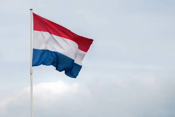 Hollanda bayrağı rüzgârda dalgalanıyor. Kırmızı, Beyaz ve Mavi. Ulusal gurur ve birlik. Hollanda 'daki vatanseverlik ruhu. Arka planda gökyüzü, su veya binalar.