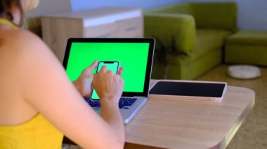 4K. Akıllı telefon yeşil ekranı kullanan bir kadın dizüstü bilgisayarı olan Chromakey 'i kapatın. Kadınların cep telefonu tutarken, yeşil ekran kaydırırken yakın plan çekimleri.