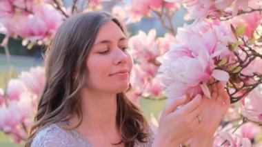 Güzel genç bir kadının bahar güzelliği portresi çiçek açan manolya çiçeği kokuyor. Bahar çiçeği. Manolya ağacının yanında giyinmiş muhteşem romantik bir kız. Yakından. Yüksek kalite.