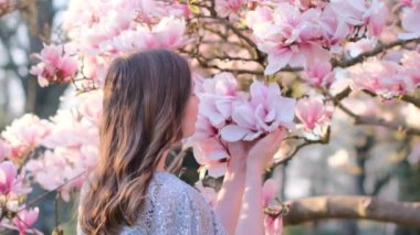 Güzel genç bir kadının bahar güzelliği portresi çiçek açan manolya çiçeği kokuyor. Bahar çiçeği. Manolya ağacının yanında giyinmiş muhteşem romantik bir kız. Yakından. Yüksek kalite.