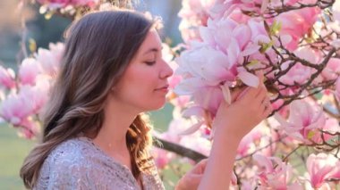 Güzel genç bir kadının bahar güzelliği portresi çiçek açan manolya çiçeği kokuyor. Bahar çiçeği. Manolya ağacının yanında giyinmiş muhteşem romantik bir kız. Yakından. Yüksek kalite.