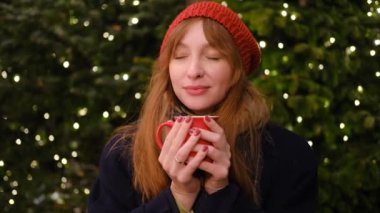 4 bin. Kırmızı bereli ve ceketli, kızıl saçlı güzel bir kadın kırmızı bardaktan sıcak çikolata içiyor ve gülümsüyor. Hight kalitesinde 4K video. 