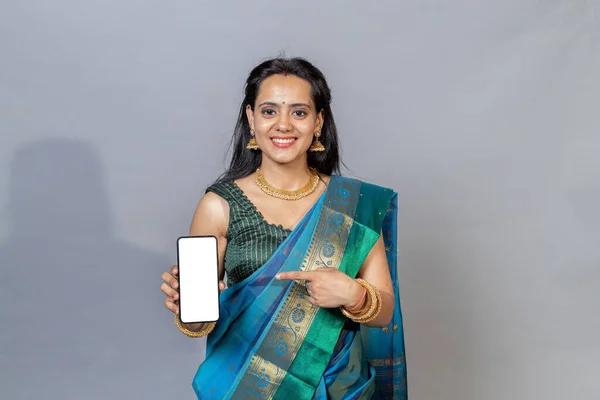 Indian woman in saree holding phone in hand looking towards the camera. Happy south Indian woman with phone looking towards the camera