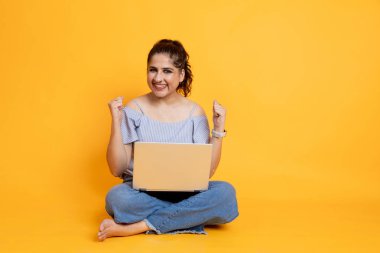 Çekici, neşeli bir kızın portresi Lotus 'ta poz veriyor. Parlak bir arkaplanda dizüstü bilgisayar kullanıyor. Teklif almaktan ve internet üzerinden kazanmaktan heyecanlanan bir kadın.