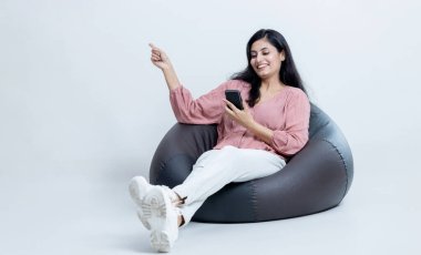 Hintli Latin kadın bir elinde telefonla fasulye çuvalında oturmuş boş yeri işaret ediyor, reklam kavramı.