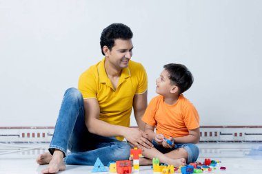 Hintli baba ve oğul yerde oturarak eğleniyorlar, aile kavramı.