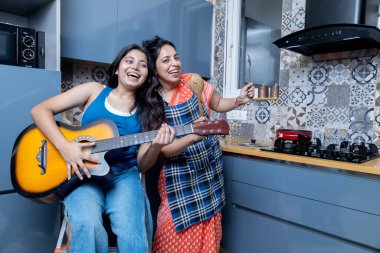 Hint anne ve kızı mutfakta yemek pişiriyor. Gitar çalan kız ve yemek hazırlayan anne.