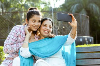 Hintli anne ve küçük kızı açık hava bahçesinde selfie çekiyorlar, annelik, anne ve kız ilişkileri gemi konsepti.