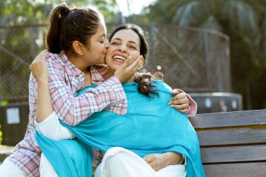 Annesine sarılan ve onu öpen mutlu Hintli kızın portresi. Anne ve kız arkadaş kavramı.