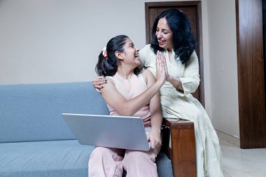 Annesiyle kanepeye oturup beşlik çakan neşeli Hintli Latin kızı, evde kanepede oturmuş beşlik çakan kız ve anne kutlarken ve beşlik çakarken