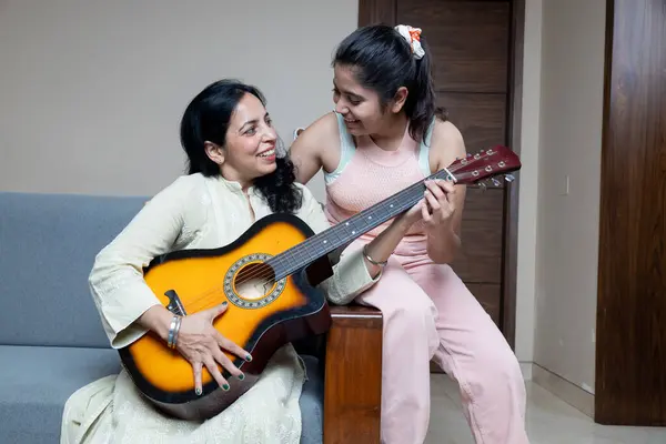 stock image Indian Young Teenage Daughter Helping mother with Guitar Playing at home sitting on sofa, Mother Daughters Relation ship