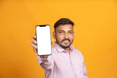 İzole edilmiş arka plandaki Hintli adam kameraya doğru boş bir telefon ekranı gösteriyor.