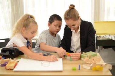 Öğretmen küçük bir çocuğa kağıt üzerinde mutlu bir şekilde resim yapmayı öğretiyor. Odaklanmış, özgüvenli, çok odaklanmış şu küçük çocuğa bakın..