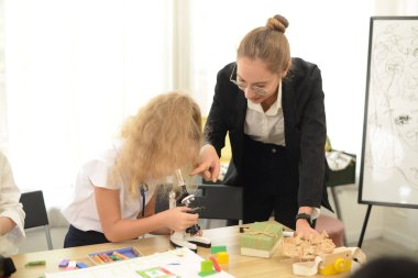 Özel hocası olan küçük bir kız biyoloji okuyor. Okul fen laboratuarında mikroskop kullanıyor..