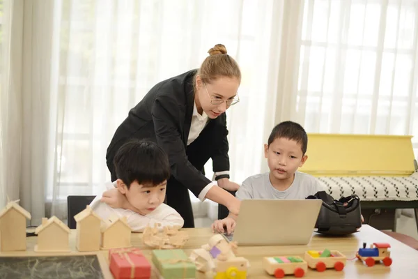 Teacher teaching her young students drawing toys or wood model on the laptop.