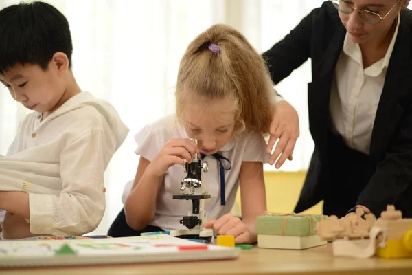 A little girl with a tutor studying chemistry that is biology using a microscope in the school science lab.