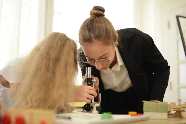A little girl with a tutor studying chemistry that is biology using a microscope in the school science lab.