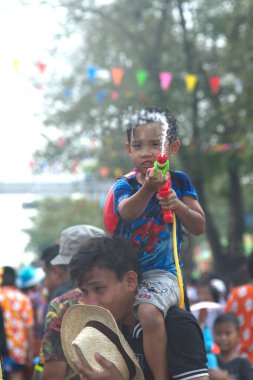 AYUTTHAYA, THAILAND - APRIL13, 2018 : An unidentified little boy rides on his father's neck playing water spray with plastic gun. Join in on the Songkran Festival, the traditional New Year celebration from April 13 to 15 in Ayutthaya , Thailand.