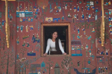 LUANG PRABANG, LAOS - 16 Mart 2023: Tanımlanamayan Asyalı kadın turistler Wat Xieng Tangası 'ndaki Pembe ibadet şapelinin penceresinde durup poz veriyorlar..