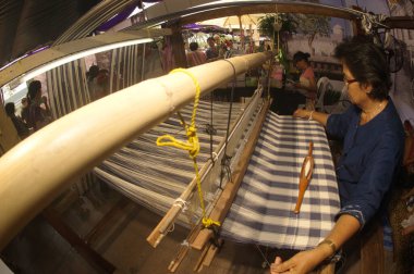 BANGKOK, THAILAND - 20 Nisan 2014: Kimliği belirsiz yaşlı bir kadın turist gösterisi için eski bir dokuma tezgahında büyük kumaşlar dokuyor. Tayland 'ın Bangkok kentindeki Rattanakosin şehrinin 232. yılındaki Tayland panayırında..