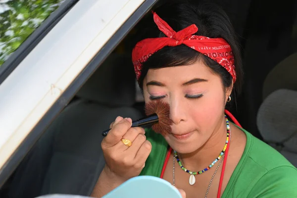 Pretty Asian female with makeup brush on her cheeks in the car.