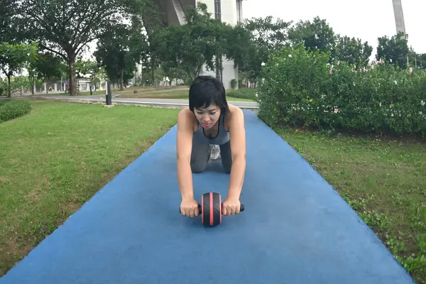 Pretty Asian woman with sports roller standing on her knees and stretching forwards on the floor during training in the park.