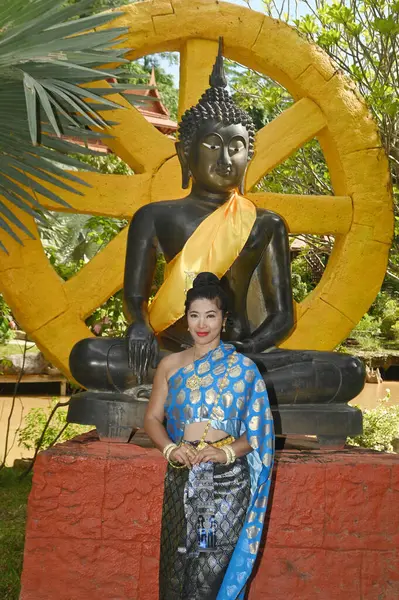 ナショナルタイの衣装のかなりアジアの女性が立って 屋外の黒い仏像の前に写真をポーズ — ストック写真
