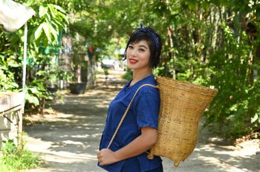 Güzel bir Asyalı kadın organik sebze tarlasının arkasında bambu sepeti taşıyor..