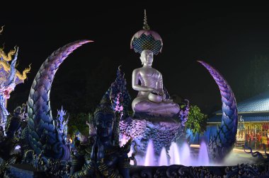 Phra Upakut 'un gece sahnesi nilüfer çiçeklerinin gölgesinin altındaki çeşmenin ortasına yerleştirilmiş inci beyazı bir heykeldir. Wat Rong Suea 10 tapınağındaki kilisenin önünde. Tayland 'ın Chaing Rai bölgesinde yer almaktadır..
