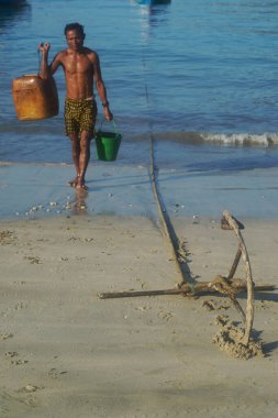 Teşekkürler, MYANMAR - 10 Aralık 2018 'de Ngapali Plajı' nın arka planında plajda plajda elinde plastik kovalarla oturan bir tekne çapası Myanmar 'ın en ünlü plajıdır. Rakhine Eyaleti 'nde Bengal Körfezi kıyısında yer alıyor. Myanmar..