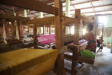 SITTWE , MYANMAR - DECEMBER 7 , 2018 : An unidentified woman working on a loom weaving using a traditional hand loom on long cotton threads.  Asian culture.