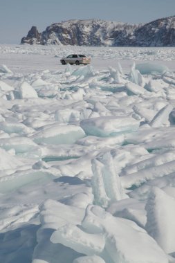 Irkutsk, Rusya - 8 Mart 2020: Tanımlanamayan bir turist Baykal Gölü 'nün buzlu yüzeyinde arabanızla seyahat ediyor. Baykal Gölü 'ndeki su kış mevsiminde tuhaf şekillerde donar. Bu manzara sadece Ocak ortasından Nisan başına kadar var olur..