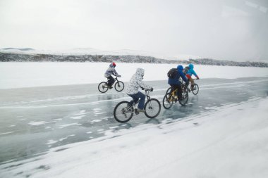 IRKUTSK, RUSSIA - 9 Mart 2020: Sırt çantalı kimliği belirsiz bir grup yolcu Baikal Gölü 'nün buzunda bisiklet sürüyor. Baykal Gölü' ndeki su kış mevsiminde tuhaf şekillerde donuyor. Bu manzara sadece Ocak ayı ortasından Nisan başına kadar var..