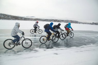 IRKUTSK, RUSSIA - 9 Mart 2020: Sırt çantalı kimliği belirsiz bir grup yolcu Baikal Gölü 'nün buzunda bisiklet sürüyor. Baykal Gölü' ndeki su kış mevsiminde tuhaf şekillerde donuyor. Bu manzara sadece Ocak ayı ortasından Nisan başına kadar var..