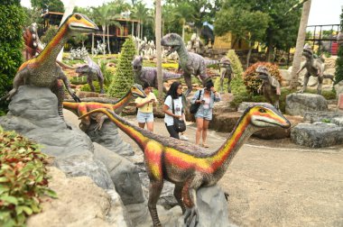 CHON BURI, THAILAND - SEPT 5, 2023: Kimliği belirsiz turistler, Nong Nooch Tropikal Bahçesi 'ndeki Dinozor Vadisi' nde çeşitli boyutlarda bir dinozor heykelini ziyaret ediyorlar..