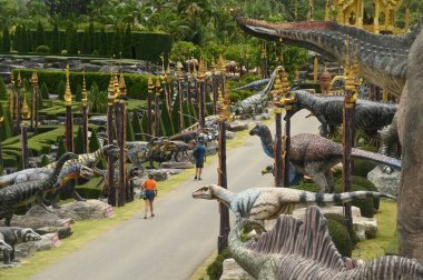 CHON BURI, THAILAND - 6 Eylül 2023: Nong Nooch Tropikal Bahçesi 'ndeki Dinozor Vadisi' nde güzel bir dinozor heykelinde ve çeşitli boyutlarda turistler.