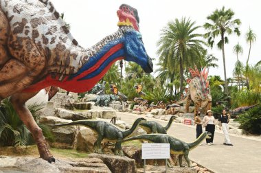 CHON BURI, THAILAND - SEPT 5, 2023: Kimliği belirsiz turistler, Nong Nooch Tropikal Bahçesi 'ndeki Dinozor Vadisi' nde çeşitli boyutlarda bir dinozor heykelini ziyaret ediyorlar..